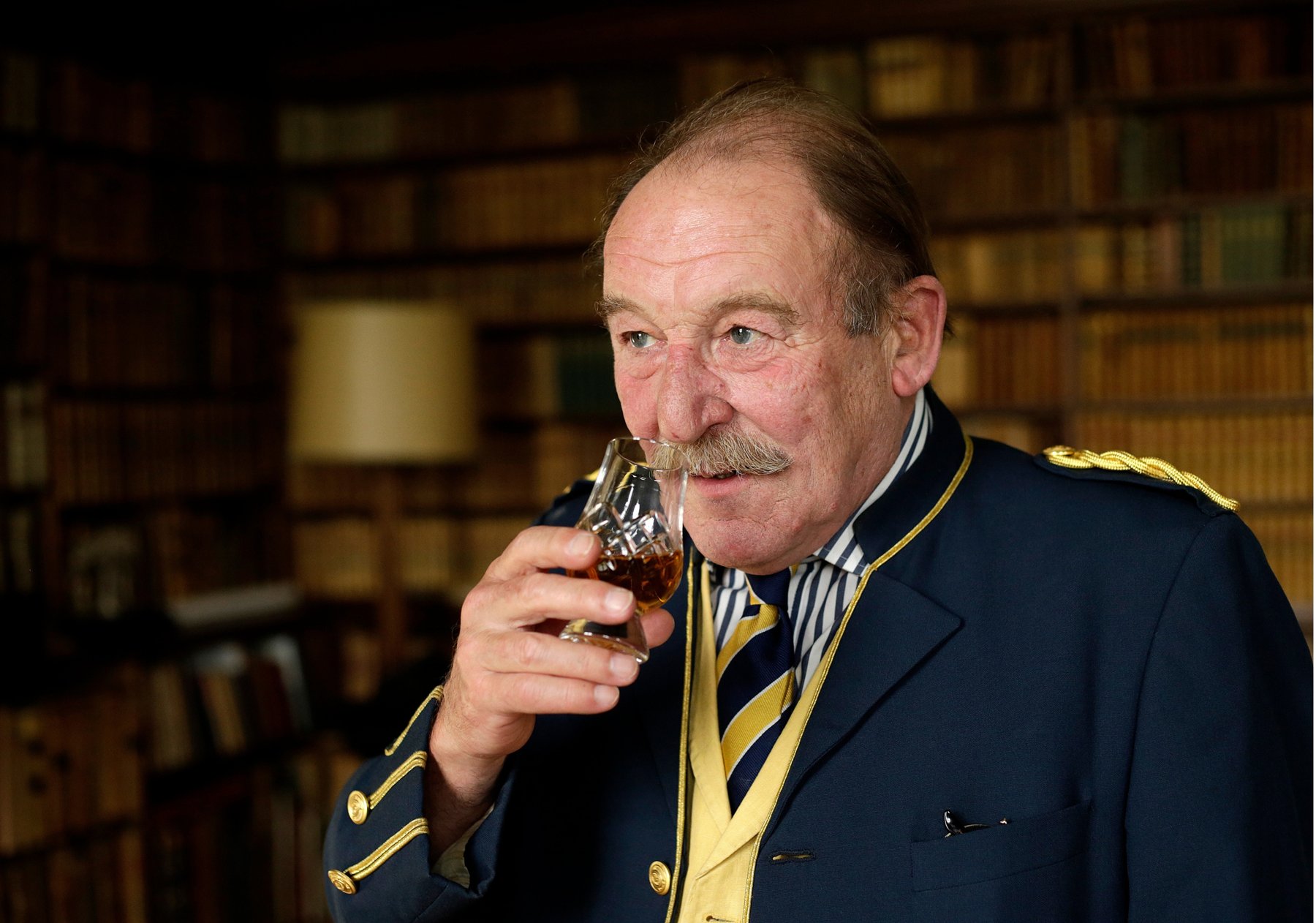 Charles MacLean MBE nosing a glass of whisky in a library