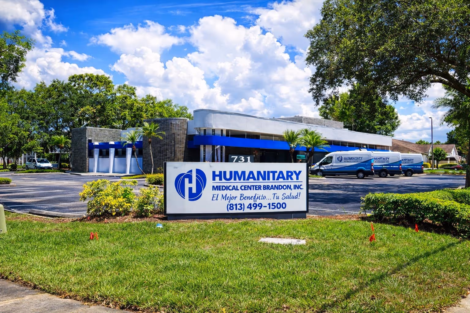 Humanitary Medical Center Brandon building with logo sign and parked vans under a blue sky with clouds.