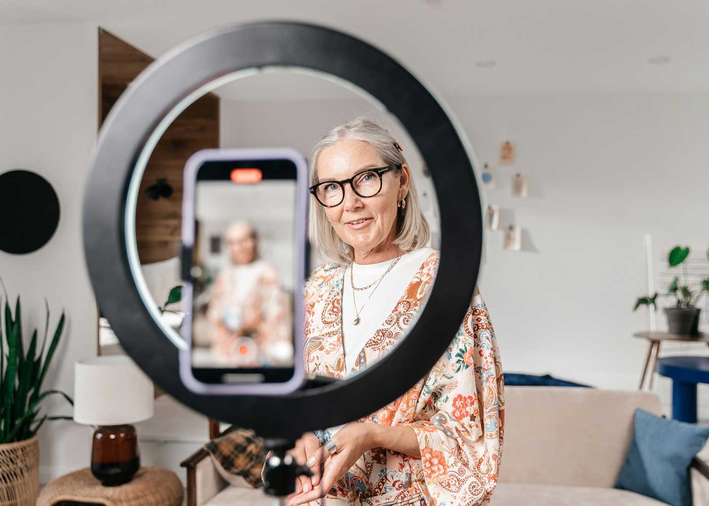 Woman looks through a ring light while recording a video on her phone.