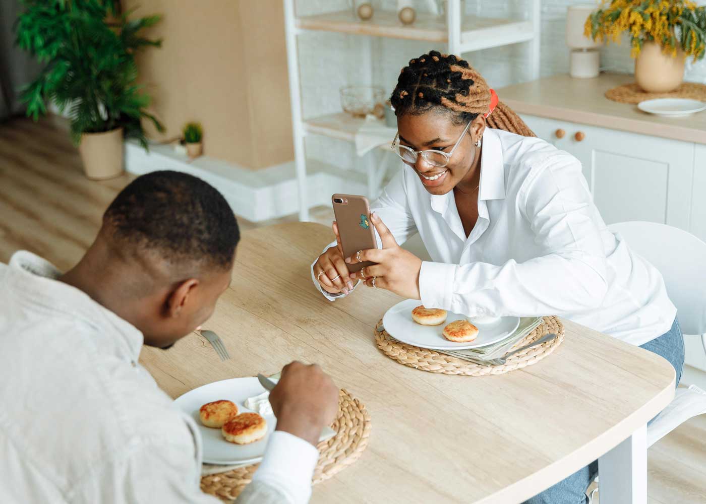 Woman uses her phone to photograph a man eating across the table from her.