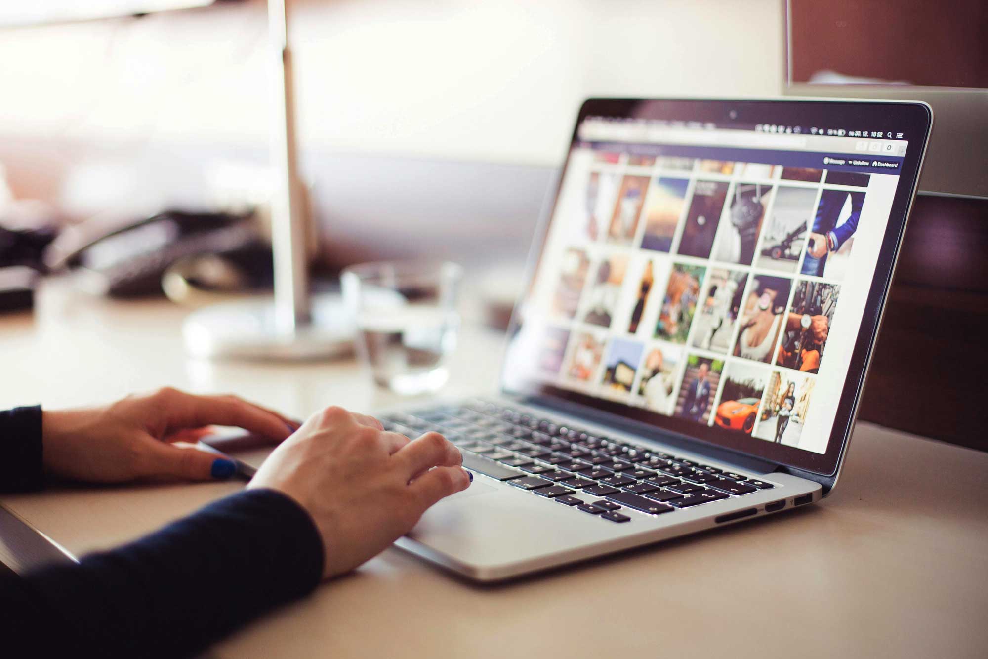 Close-up of a person's hands scrolling on a laptop. On the screen is a gallery of photos they're browsing.