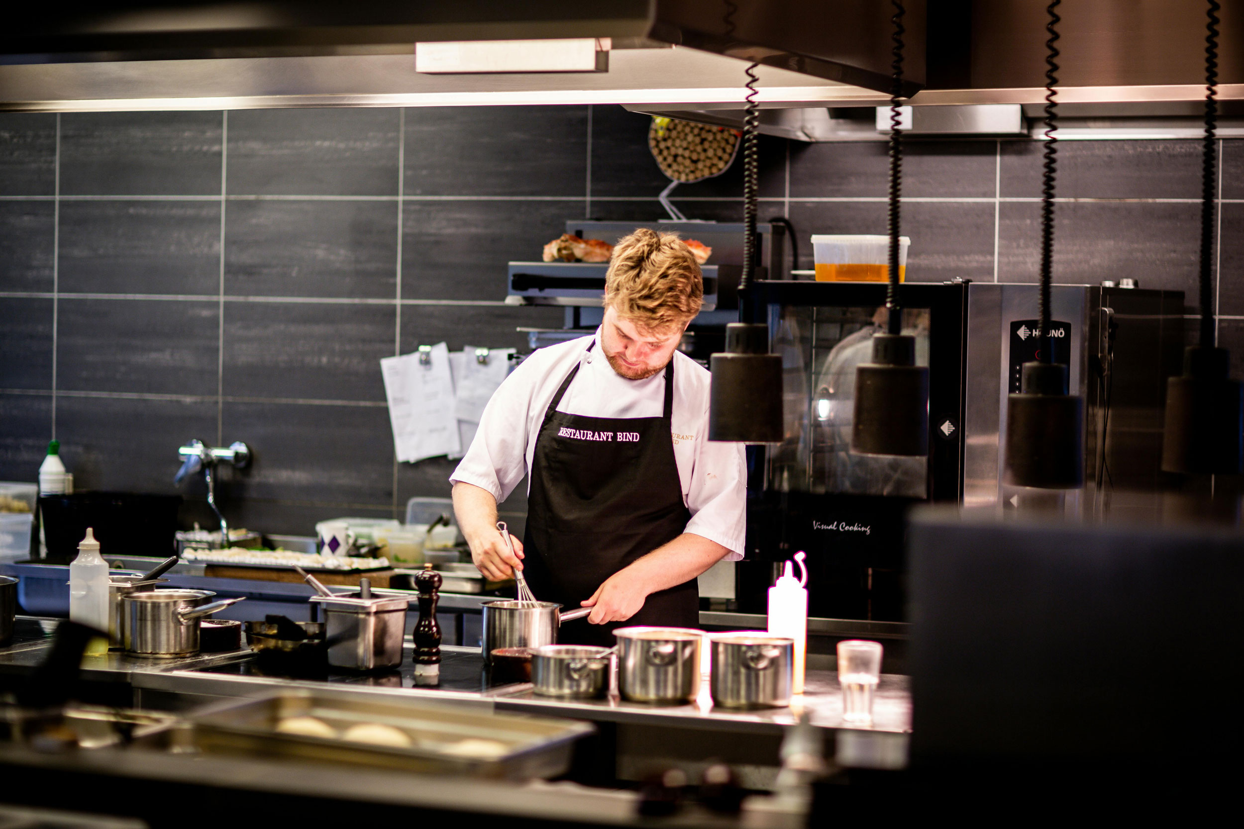 Professional chef whisks ingredients together in a metal sauce pan in the kitchen of Restaurant Bind in Sønderhav, Denmark.