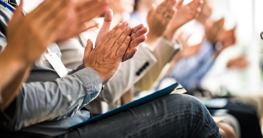 a row of a seated audience clapping at a live event