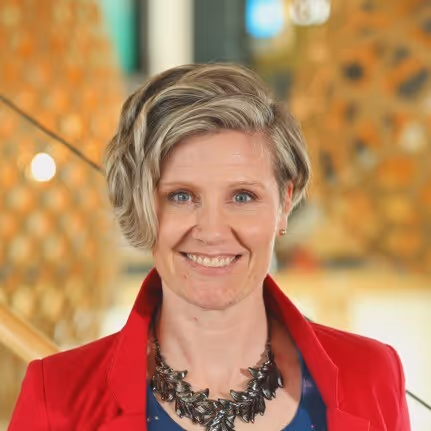 A woman in a red jacket smiles at the camera.