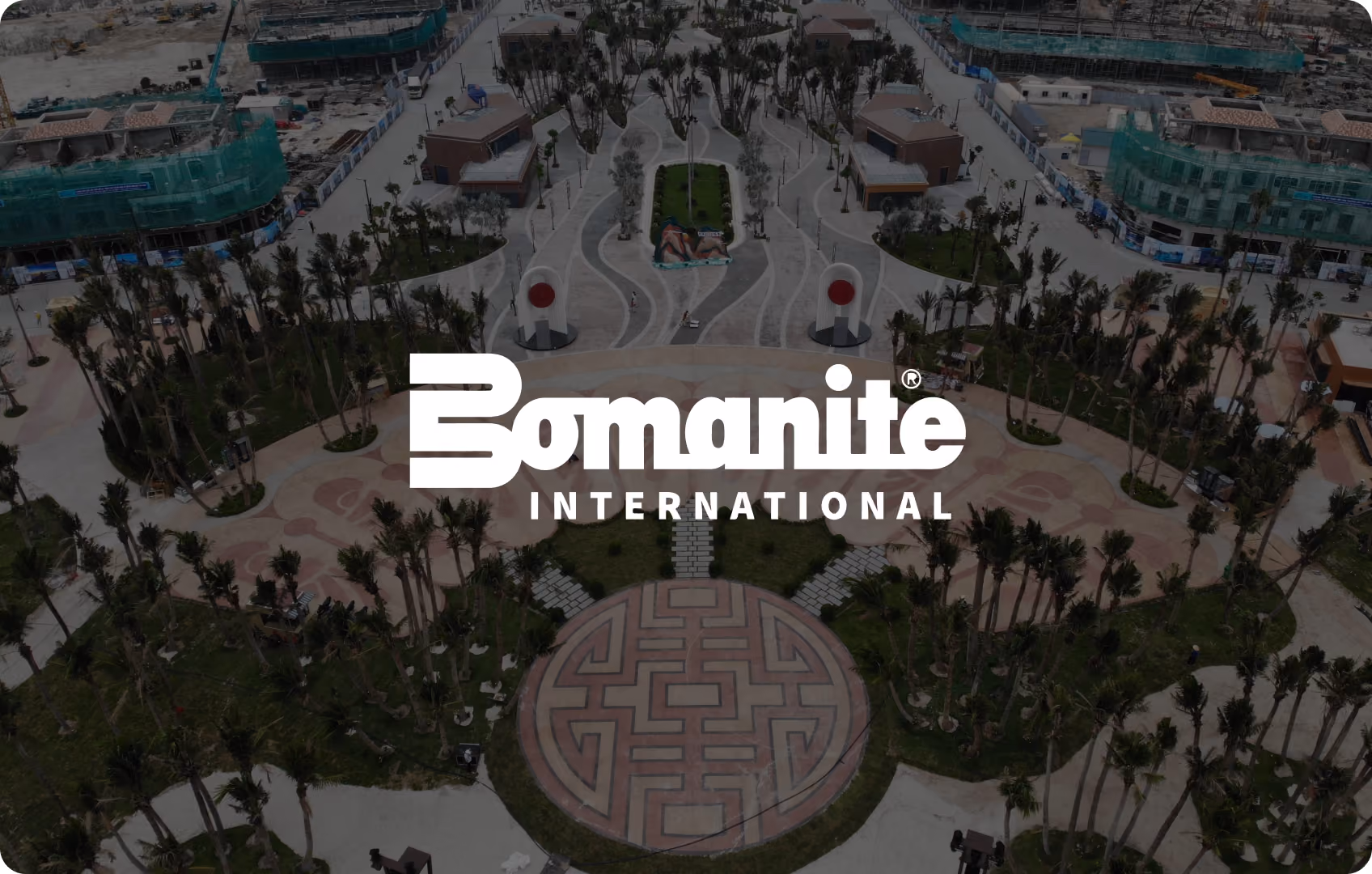 Aerial view of landscaped park with palm trees, patterned circular plaza, and surrounding construction.