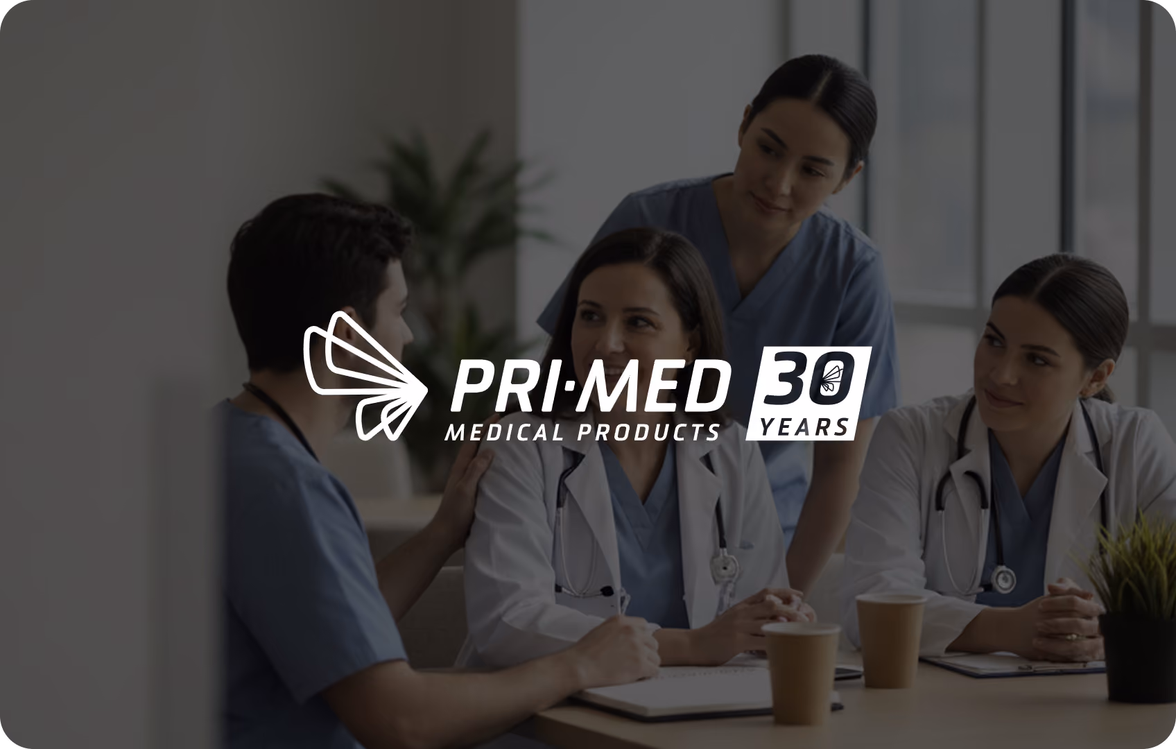 Four medical professionals in discussion at a table with coffee cups and notebooks.