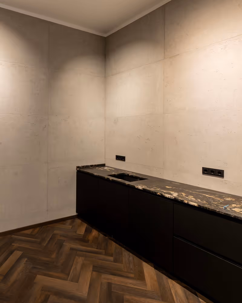 Moderne Küche mit dunklem Holzparkettboden, schwarzen Unterschränken und einer marmorierten Arbeitsplatte mit integriertem Spülbecken.