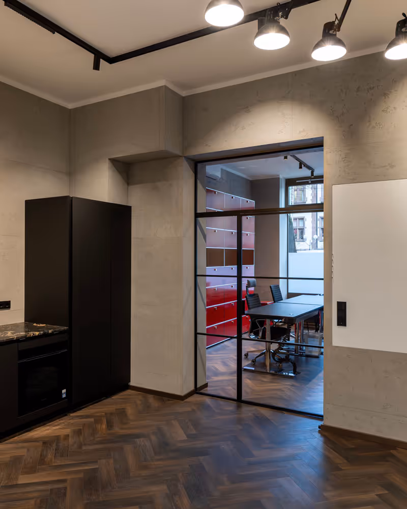 Moderner Büroraum mit Holzparkettboden, schwarzen Möbeln und Glaswand, die in einen Besprechungsraum mit roten Schränken führt.