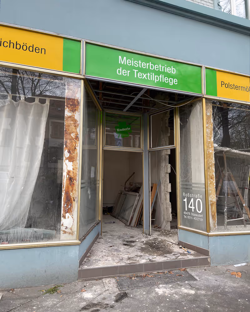 Eingang eines Ladengeschäfts mit Schild 'Meisterbetrieb der Textilpflege', verfallene Fassade und Baustelle im Inneren.