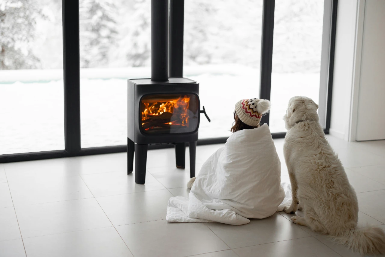 A woman and dog bundled up by a fire in the winter