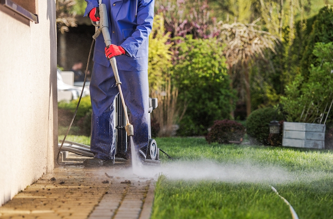 Caucasian Men and the Spring Maintenance and Cleaning. Washing House Backyard Brick Paths Using Pressure Washer. House Surroundings Maintenance. Housing Theme.