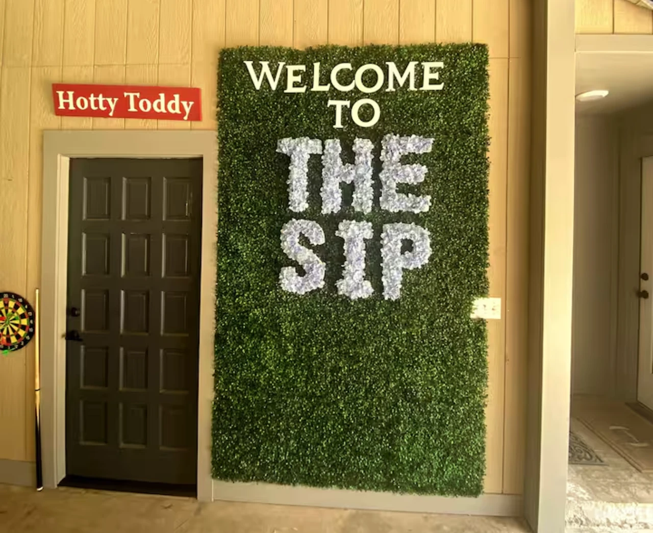 Ole Miss-themed entry at the Oxford Airbnb with a 'Welcome to The Sip' greenery wall and a Hotty Toddy sign