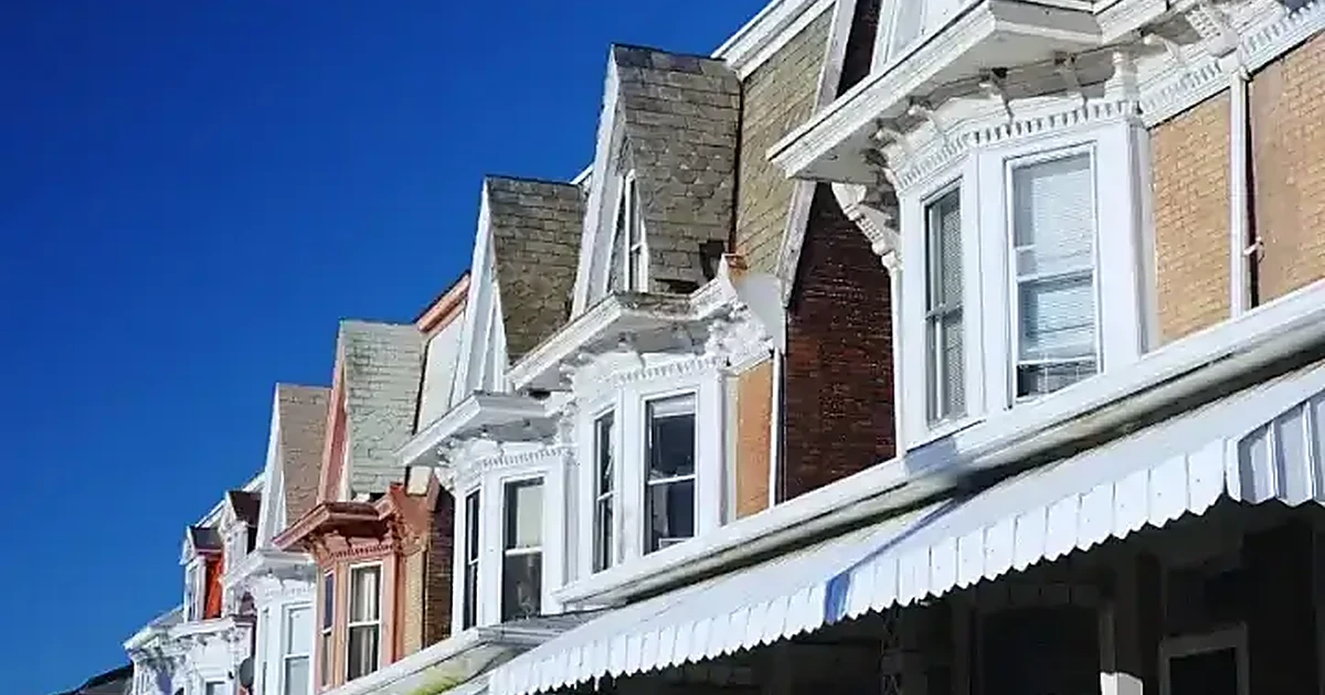 Row of Pennsylvania rowhomes with ornate white cornices and gabled roofs against a clear blue sky