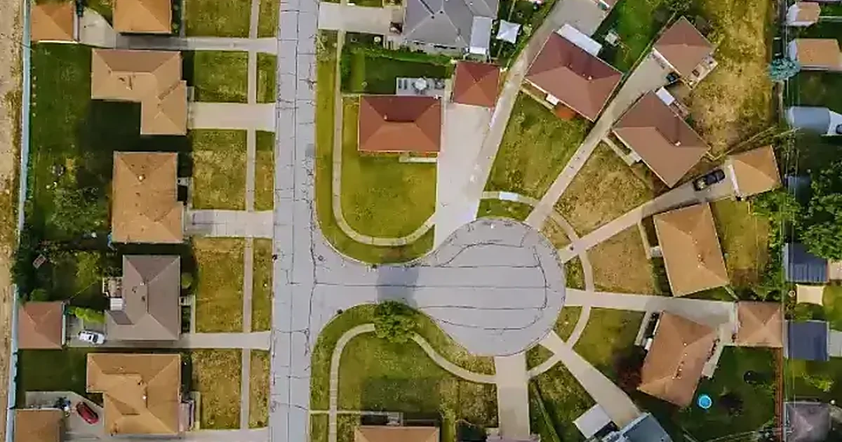 Aerial view of a suburban cul-de-sac lined with detached homes, lawns and sidewalks