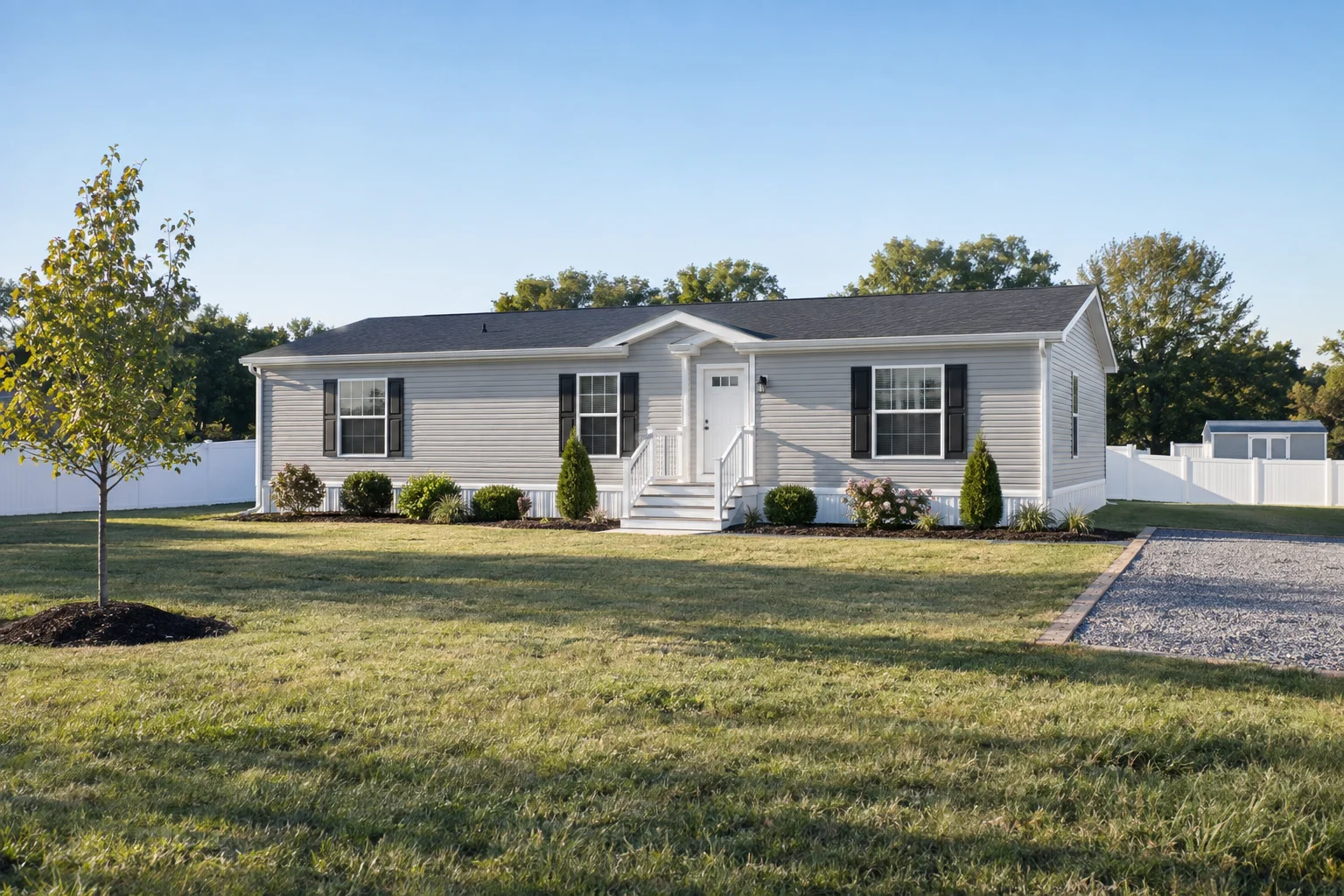 Single-story manufactured home with white siding and black shutters on a landscaped lot