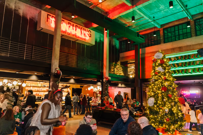 Holiday party guests gathered beside a lit Christmas tree under red and green lighting