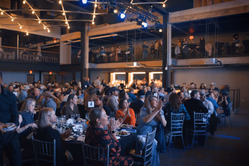 Corporate dinner seated at round tables beneath the mezzanine and string lights