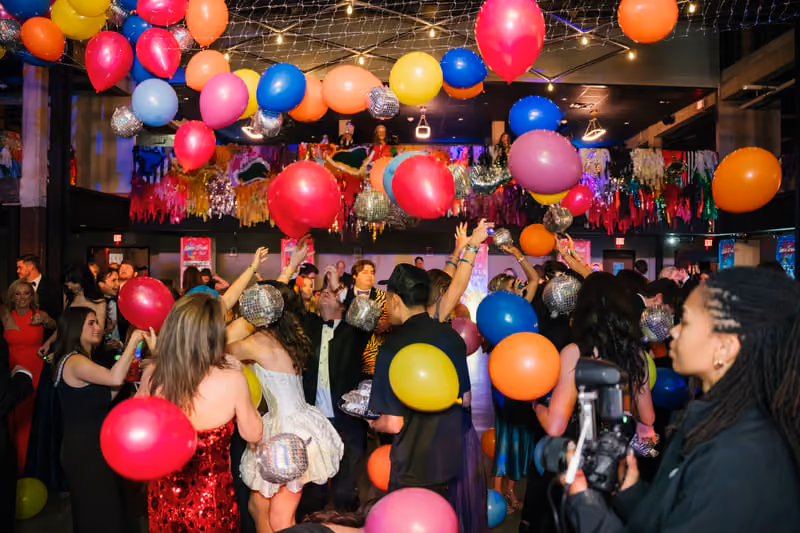 Birthday party guests dancing under a ceiling filled with balloons and metallic streamers
