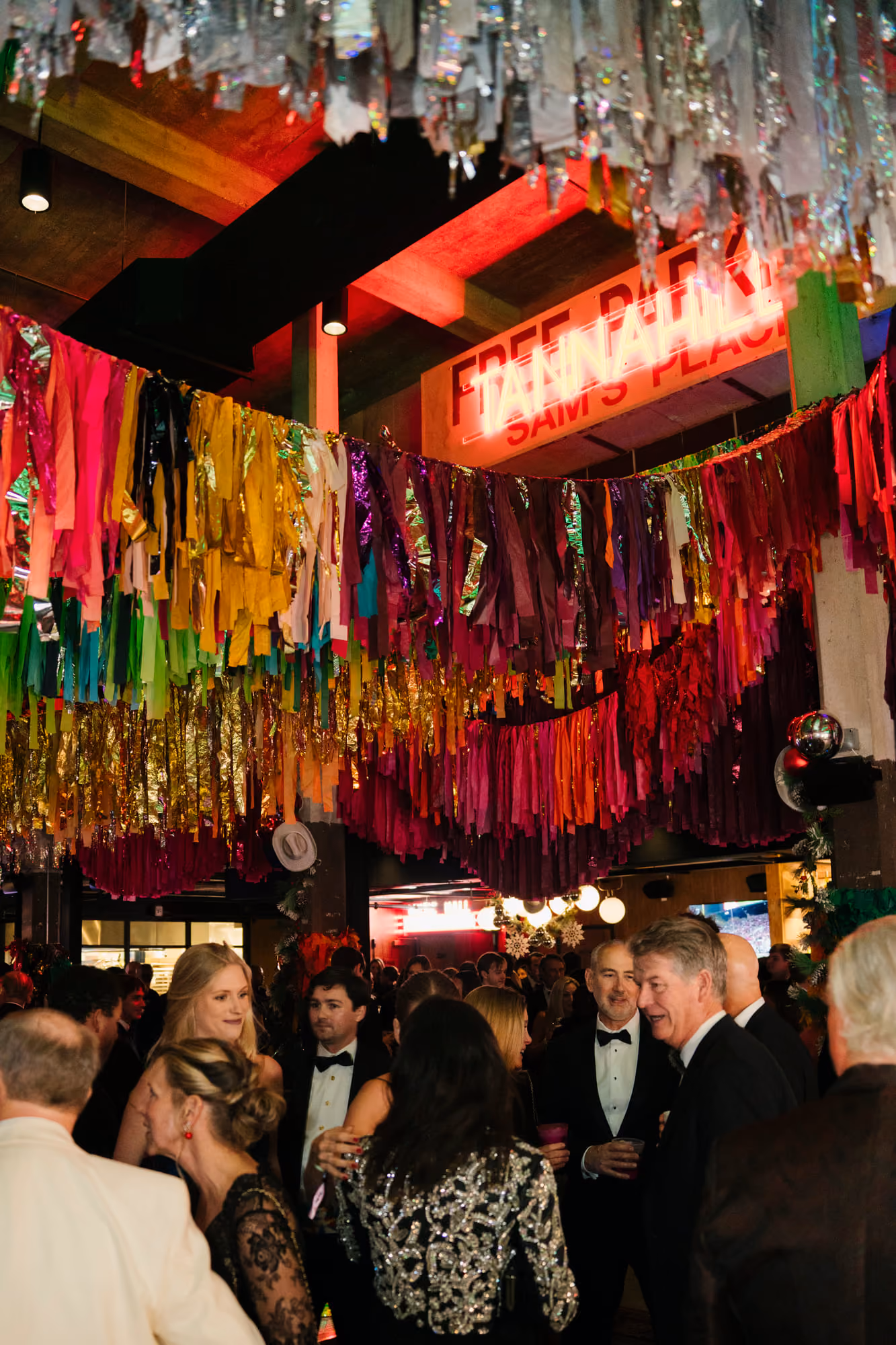 Black-tie guests mingling beneath a ceiling of colorful fringe garland at Tannahill's