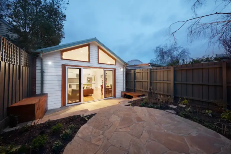 Modern home extension with large glass doors opening to a stone patio and garden area at dusk.