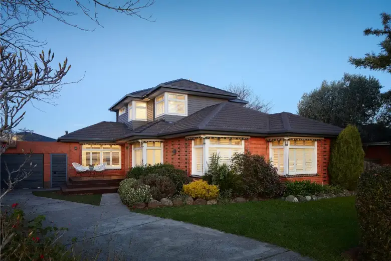 Brick home with an upper-storey weatherboard extension, dark tiled roof, and landscaped front garden.