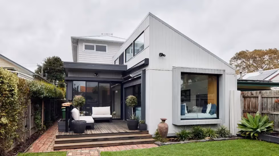 Contemporary two-storey home extension with large windows, timber deck, and landscaped backyard.