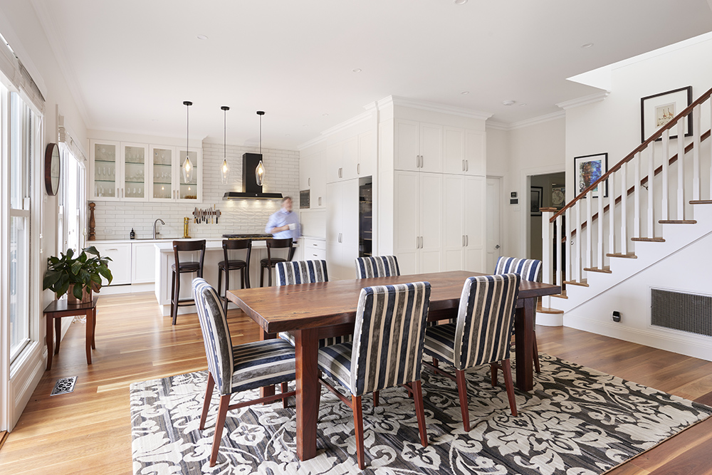 A bright, open-plan dining and kitchen area with polished timber floors. A wooden table with striped chairs sits on a patterned rug.