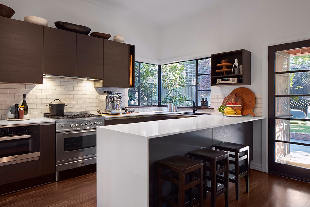 A modern kitchen with dark brown cabinets, white subway tile backsplash, stainless steel appliances, and a central white island with dark stools.]