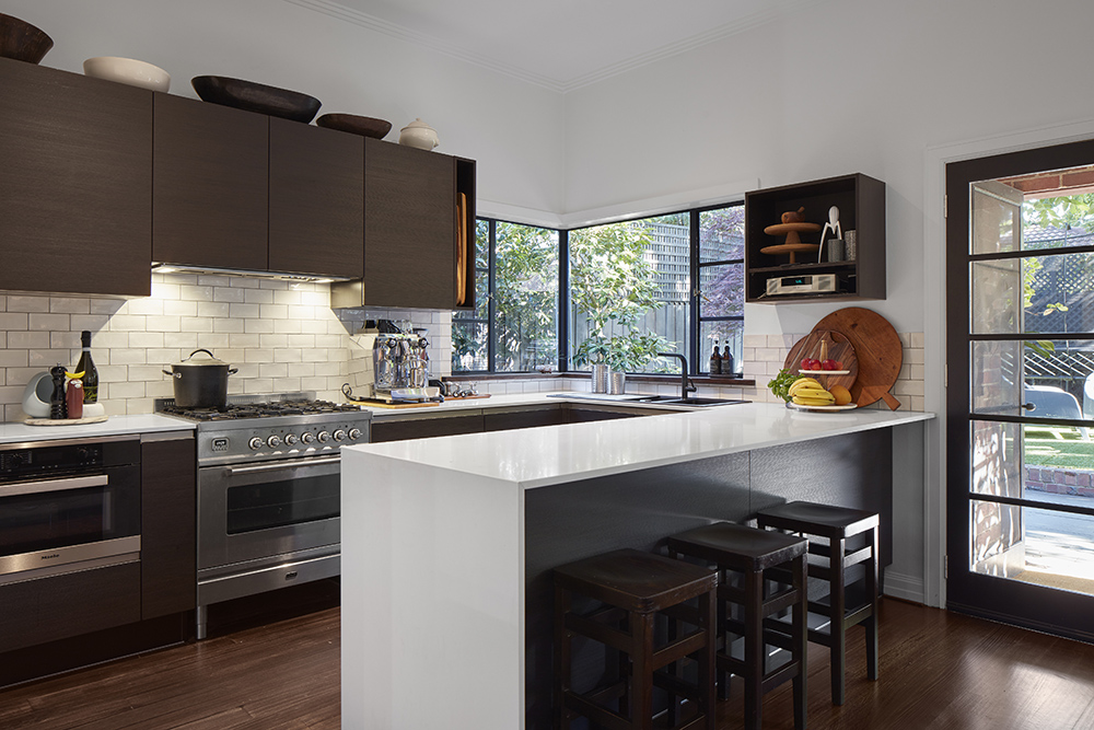 A modern kitchen with dark brown cabinets, white subway tile backsplash, stainless steel appliances, and a central white island with dark stools.]