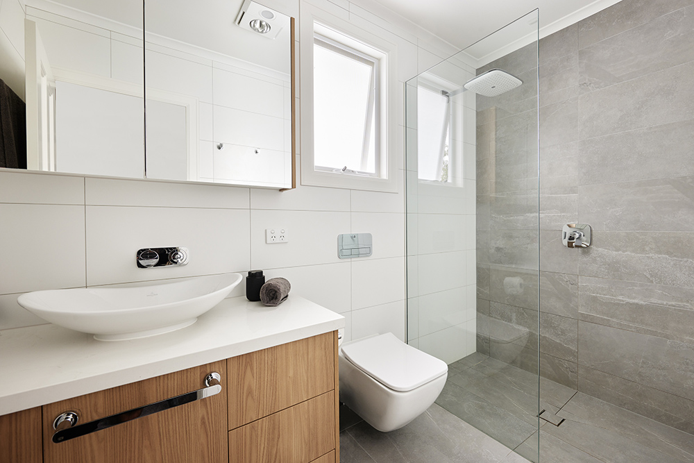 Modern, minimalist bathroom with a wood vanity, white vessel sink, mirrored cabinet, and a frameless glass walk-in shower.