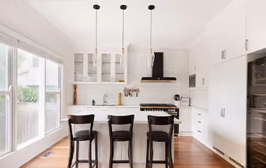 Modern white kitchen renovation with a central island, timber flooring and contemporary cabinetry.