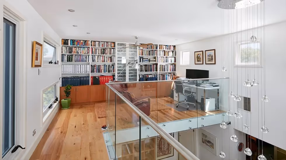 Modern upper-storey extension featuring a home office, library shelving and a glass balustrade overlooking the lower level.