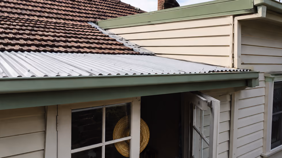 Exterior view of a weatherboard home showing a corrugated metal awning adjacent to a tiled roof line and glass door.