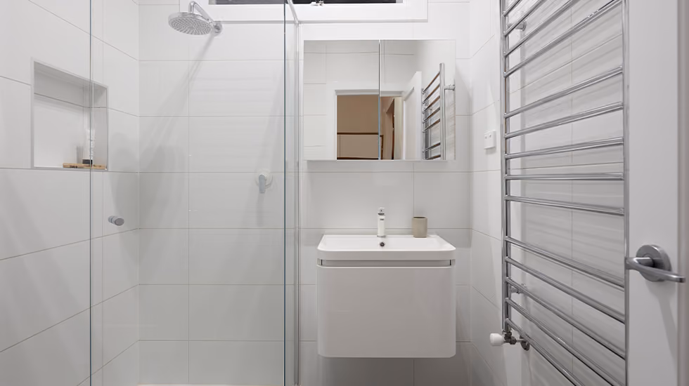 Modern white bathroom featuring a glass-enclosed shower, wall-hung vanity, mirror cabinet, and heated towel rack.