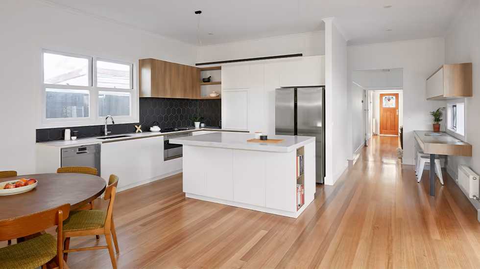 Modern open-plan kitchen and dining area with white cabinetry, timber accents, stainless steel appliances, a central island and warm timber flooring.