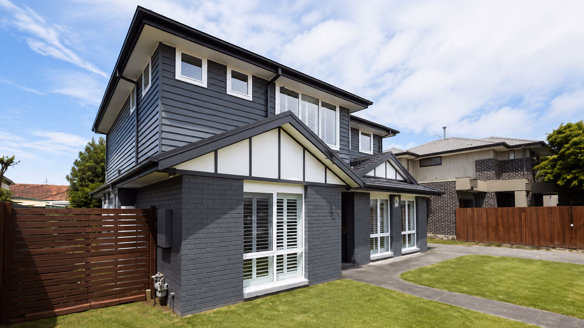 A modern two-storey dark grey brick and weatherboard house with white window frames and a neat green lawn on a sunny day.
