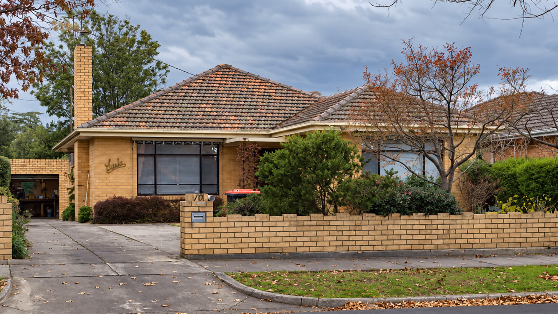 Original post-war cream brick house with a tiled roof and matching brick fence.