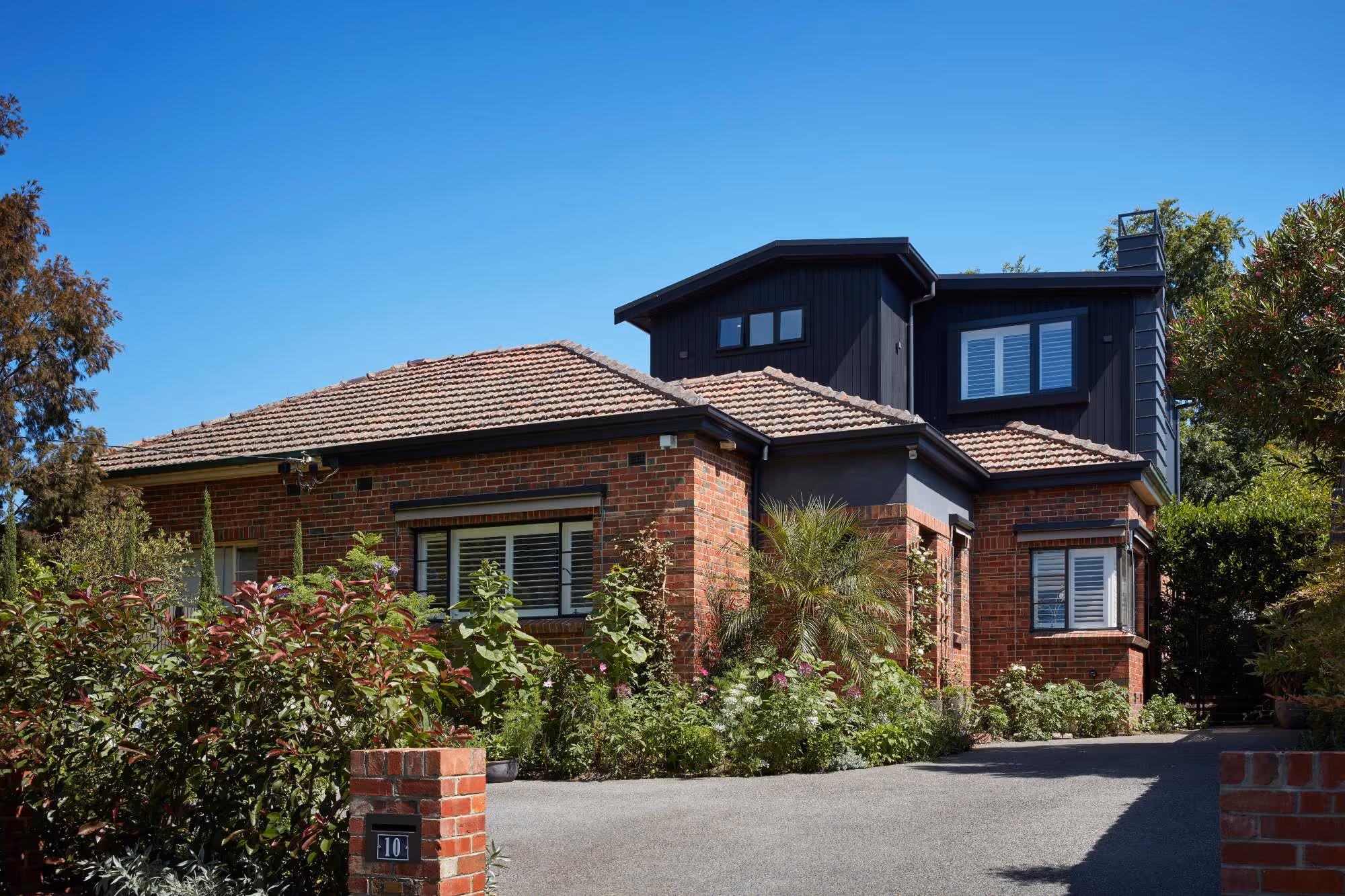 Brick house with modern upper level and garden-lined driveway.