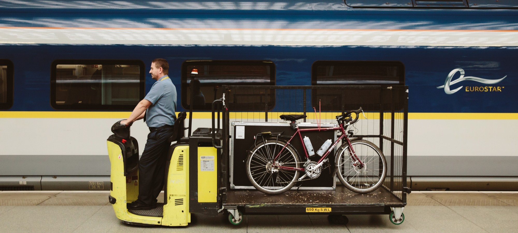 A luggage car carring a bike along a station platform in front of a Eurostar train.