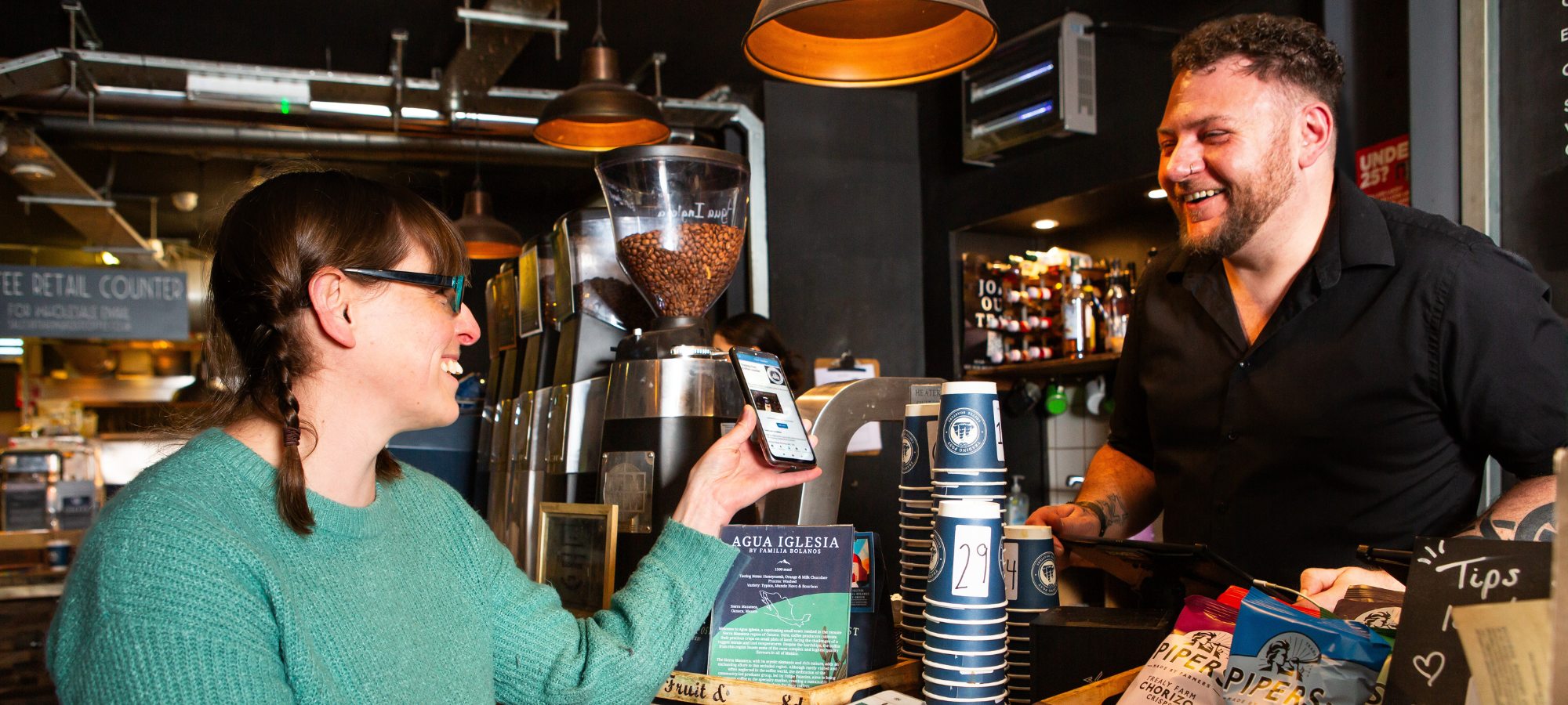 A lady showing a voucher on her phone to a barista in a cafe