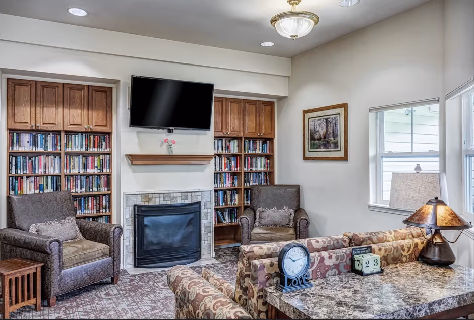 Over 55 Communities in Granite Falls, WA - The Village at Granite Falls - Clubhouse with Sofa, Armchairs, Fireplace, Bookshelves, and Wall-Mounted TV.