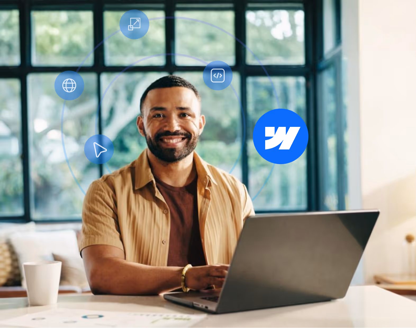 Smiling man sitting at a table with a laptop, surrounded by digital icons representing internet and coding.