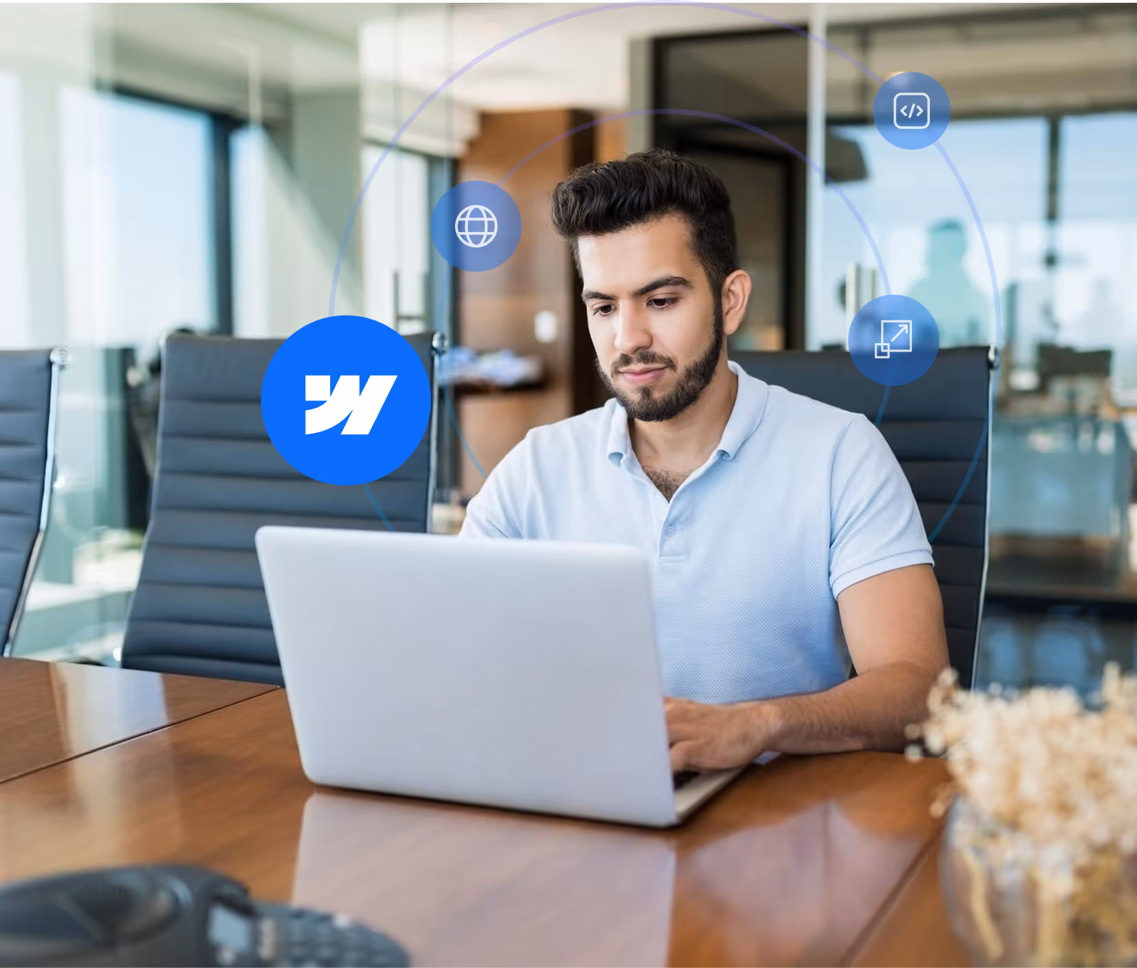 Man with beard working on a laptop in a modern office conference room with digital icons around him.