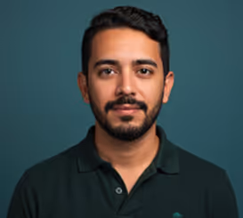 Portrait of a man with short dark hair and beard wearing a dark green polo shirt against a plain blue background.