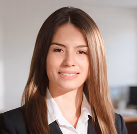 Smiling young woman with long straight brown hair, wearing a black blazer and white collared shirt.