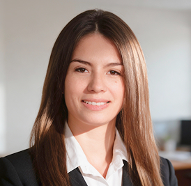 Smiling young woman with long straight brown hair, wearing a black blazer and white collared shirt.