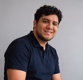 Smiling man with short curly hair wearing a dark blue polo shirt against a gray background.