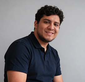 Smiling man with short curly hair wearing a dark blue polo shirt against a gray background.