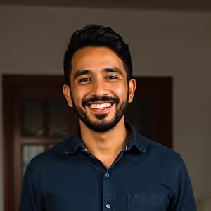 Smiling man with dark hair and beard wearing a dark blue button-up shirt against a blurred indoor background.