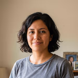 Smiling woman with short dark hair wearing a gray t-shirt in a cozy indoor setting.